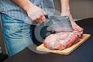 Piece of pork neck cutout on woodwn table. Man cutting meat