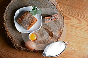Piece of poured honey cake with cream on plate, decorated with anise and a bunch of mint, eggs, milk, sticks of cinnamon and cocoa