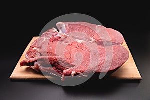 piece of raw beef in a slice on a wooden cutting board, on a black background. Procuring food