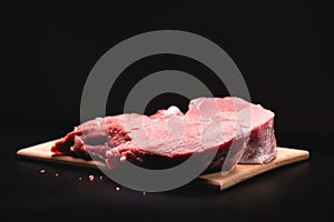 piece of raw beef in a slice on a wooden cutting board, on a black background. Procuring food