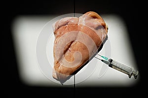 Piece of raw meat injected with hormones using needle and syringe