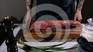 a piece of raw meat lies on the cutting board in front of the cook in the kitchen.