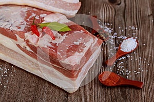 Piece of raw pork belly with salt and red paprika on wooden table