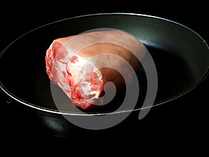 A piece of raw pork knuckle in a pan