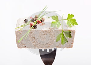 Piece of raw tofu on silver fork, decorated with spices and herb, white background