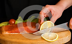 A piece of red fish on a wooden board, knife lies on the table near the fish