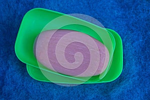 A piece of red soap in a plastic green soap dish on blue matter