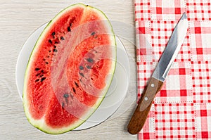 Piece of red watermelon in white plate, knife on napkin on wooden table. Top view