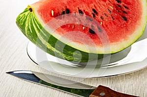 Piece of red watermelon in white plate, knife on wooden table