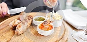 A piece of sausage is dipped in sauce. Lunch in a restaurant, a woman cuts Grilled sausages. Barbecue restaurant menu, a