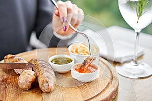 A piece of sausage is dipped in sauce. Lunch in a restaurant, a woman cuts Grilled sausages. Barbecue restaurant menu, a