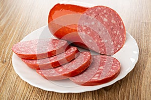 Piece of sausage, slices of sausage in plate on wooden table