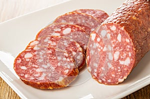 Piece and slices of smoked sausage in plate on wooden table