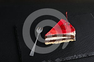 Piece of sponge cake with maraschino cherry and fork on black background