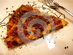 A piece of super deluxe pizza with spices and silver fork, that