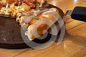 Piece of super deluxe pizza on wooden tray on wooden table with scoop, Traditional Italian fast food.