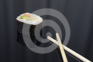 a piece of sushi with chopsticks in dark background