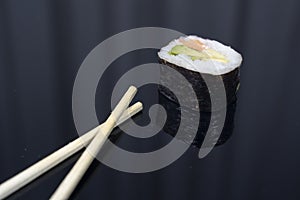 a piece of sushi with chopsticks in dark background