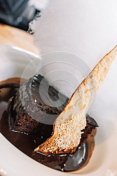 Piece of tasty chocolate cake on melted chocolate and sugar cloud served on white plate. Dessert background