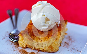 Piece of tasty vegan orange cake with vanilla ice cream served on white board