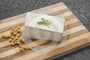 A piece of tender tofu and soybeans on a wooden cutting board