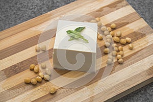 A piece of tender tofu and soybeans on a wooden cutting board