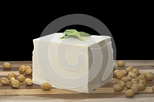 A piece of tender tofu and soybeans on a wooden cutting board