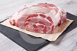 A piece of uncooked meat of pork neck on black stome plate on gray table. Close up view photo