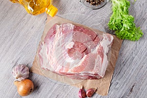 A piece of uncooked meat of pork neck on black stome plate with ingredient on gray table. Ready to be coocked. Top view photo