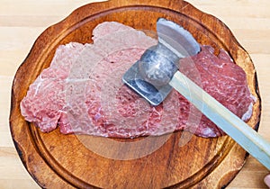 Piece of veal is beating by meat mallet