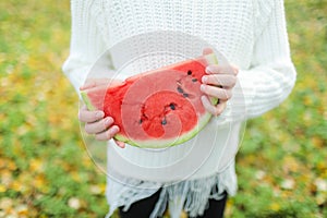 A piece of watermelon in the hands of a girl on an autumn day