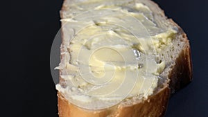 A piece of white bread and butter rotates on a black background