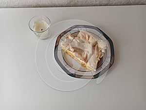 A piece of white cake on a plate. On a light background near a white wall