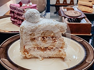 Piece of white cake with sponge cake, coconut flakes and decoration on top of the cake in the form of a ball on a plate in a