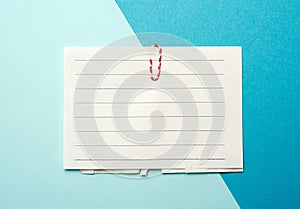 Piece of white paper in a line and a red paper clip on a blue background