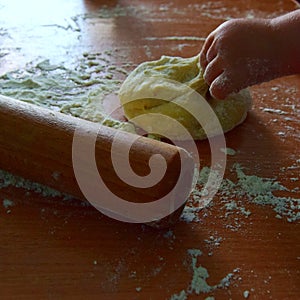Piece of yeast dough in the home kitchen with a rolling pin and flour and a small childs hand. Close up. Soft focus