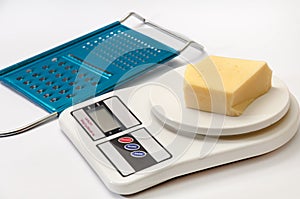 A piece of yellow cheese on a kitchen digital scale with grater