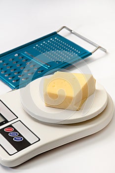 A piece of yellow cheese on a kitchen digital scale with grater