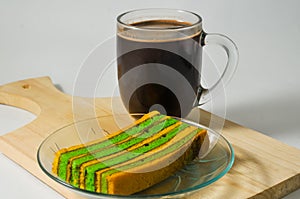A piece of yellow-green lapis legit cake with a glass of coffee