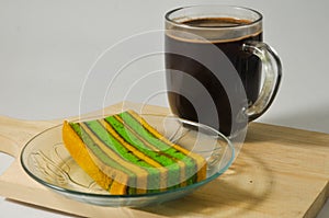 A piece of yellow-green lapis legit cake with a glass of coffee