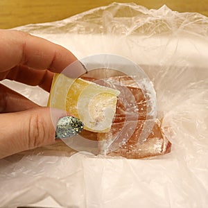 A piece of yellow Locum with powdered sugar in a woman`s hand against a background of pink Locum pieces in a box.