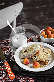 Pieces of apricot pie on a white plate, bowl with apricots and a jar of natural yoghurt on the table