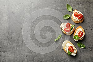 Pieces of baguette with tasty cream cheese and tomatoes on gray table, flat lay.