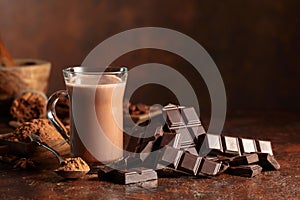 Pieces of bitter chocolate and glass of cocoa drink on a brown table