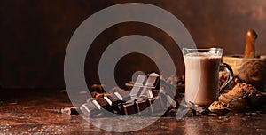 Pieces of bitter chocolate and glass of cocoa drink on a brown table