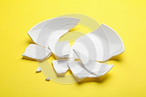 Pieces of broken ceramic plate on yellow background