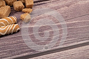 Pieces of brown cane sugar and cookie sticks with chocolate and white icing on a wooden background. Close up