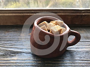Pieces of brown sugar in a ceramic mug on a wooden background