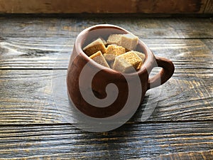 Pieces of brown sugar in a ceramic mug on a wooden background