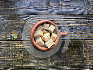 Pieces of brown sugar in a ceramic mug on a wooden background